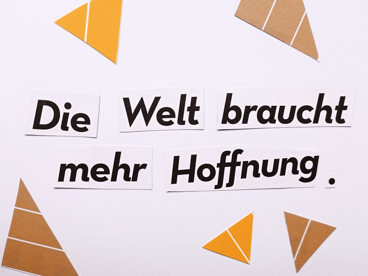 Inspirational text Die Welt braucht mehr Hoffnung on a white background with triangle cutouts.